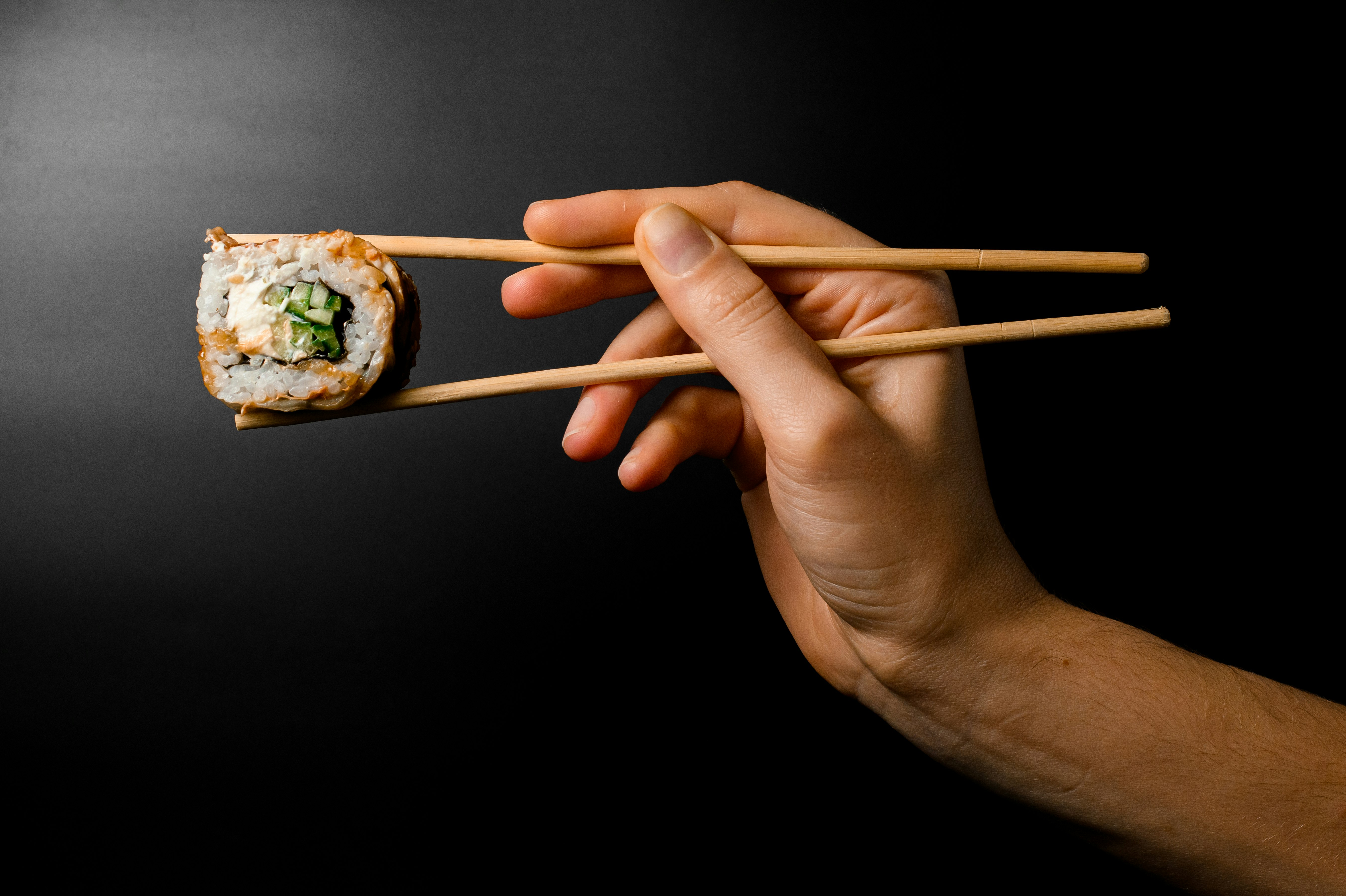 Sushi held with chop sticks on black background