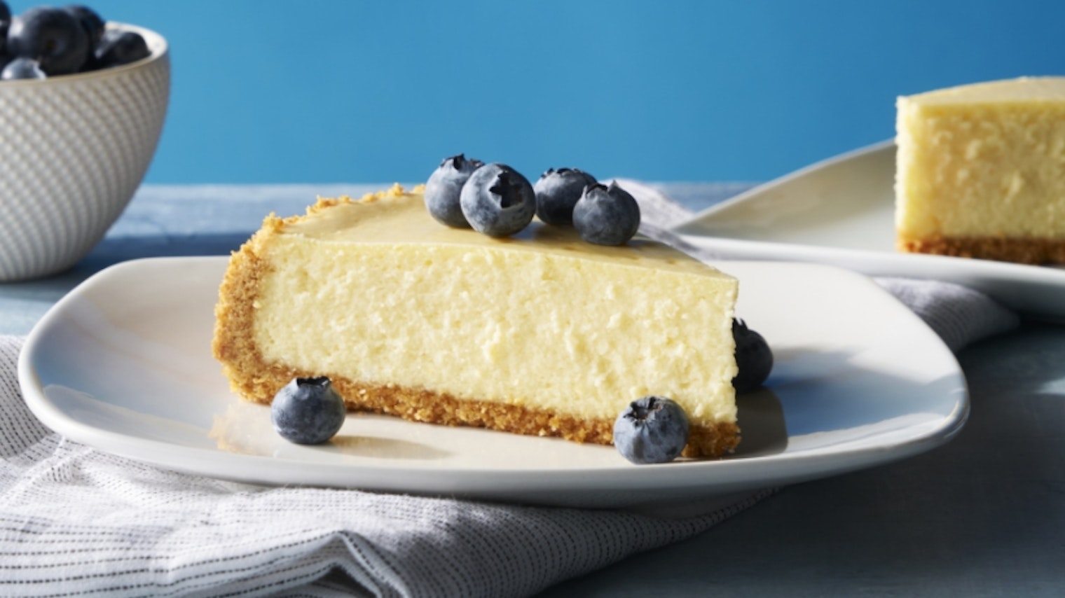 Cheesecake with blueberries on plate with blue background