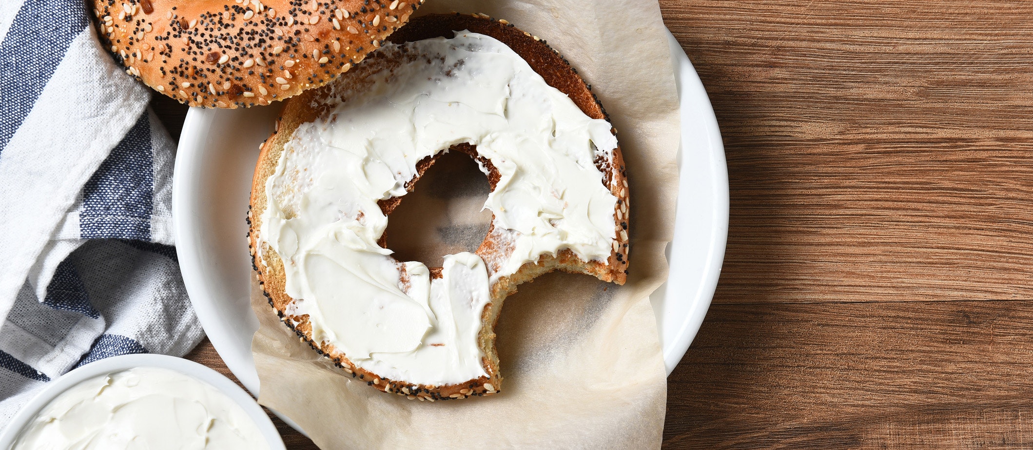 A bagel with cream cheese on a plate and a bite taken out. On a rustic wood table with copy space.
