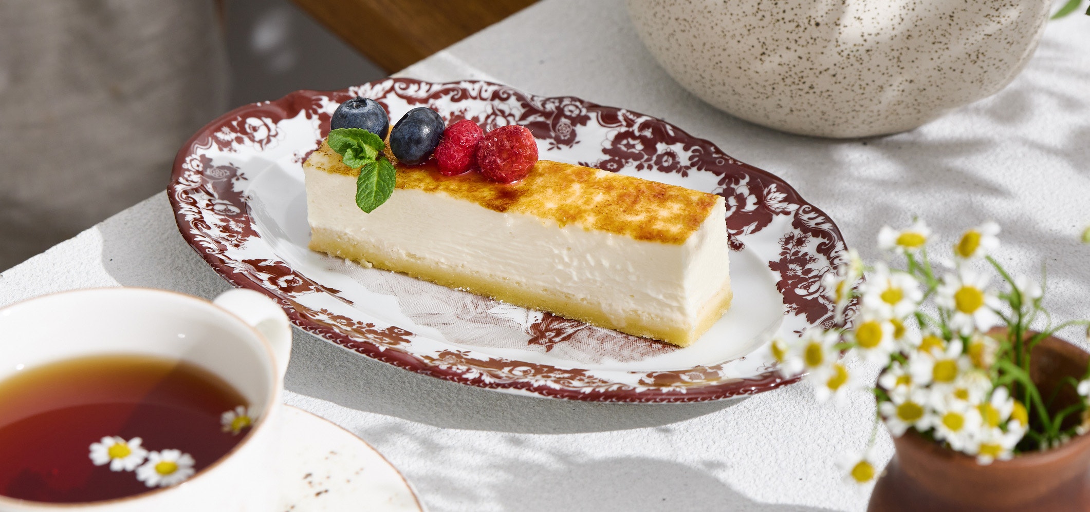 Cheesecake slice with berries on vintage plate, bright natural lighting, angled composition.