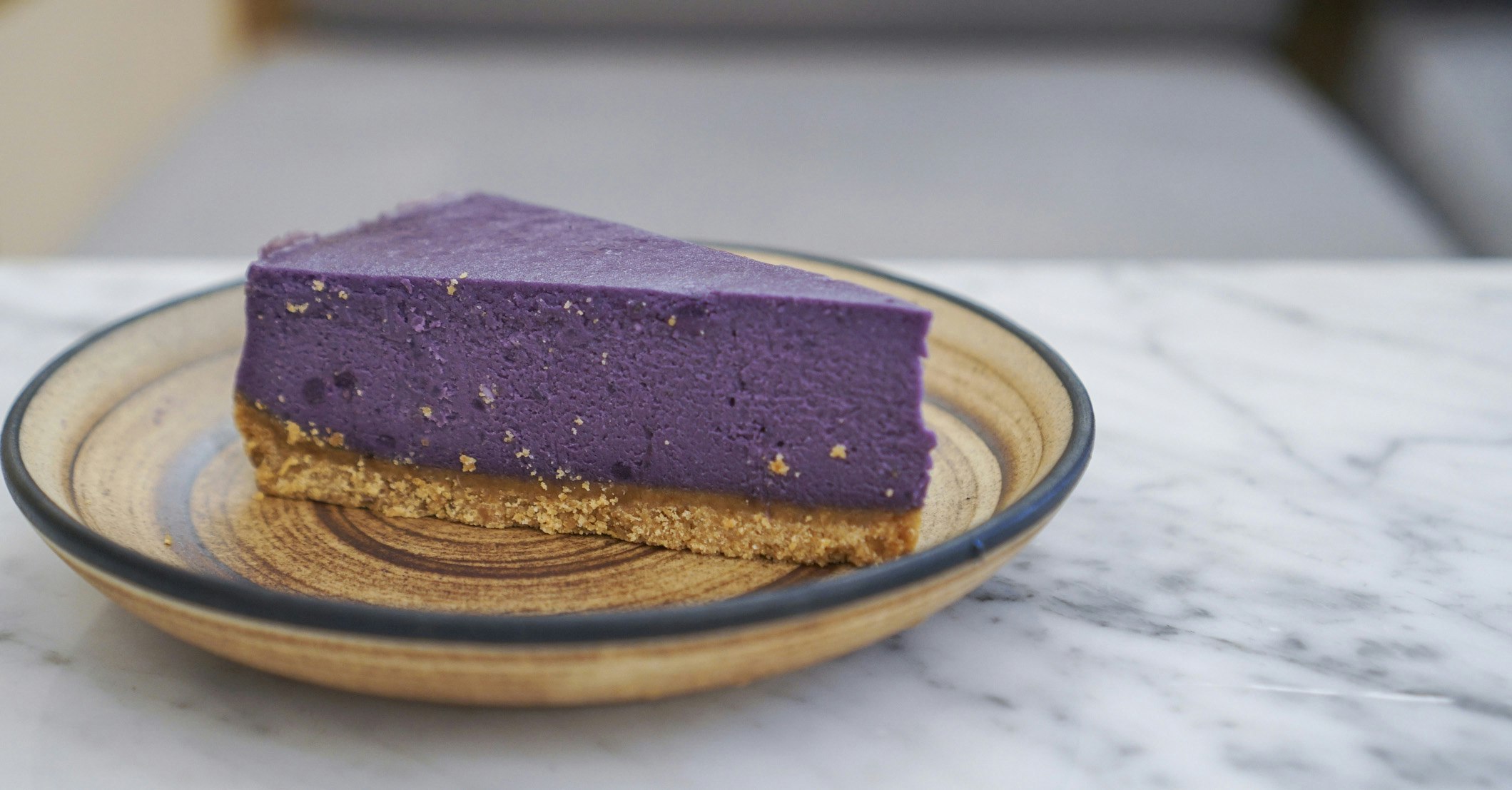 A piece of purple sweet potato cheesecake with crumble cookies crust on ceramic plate.